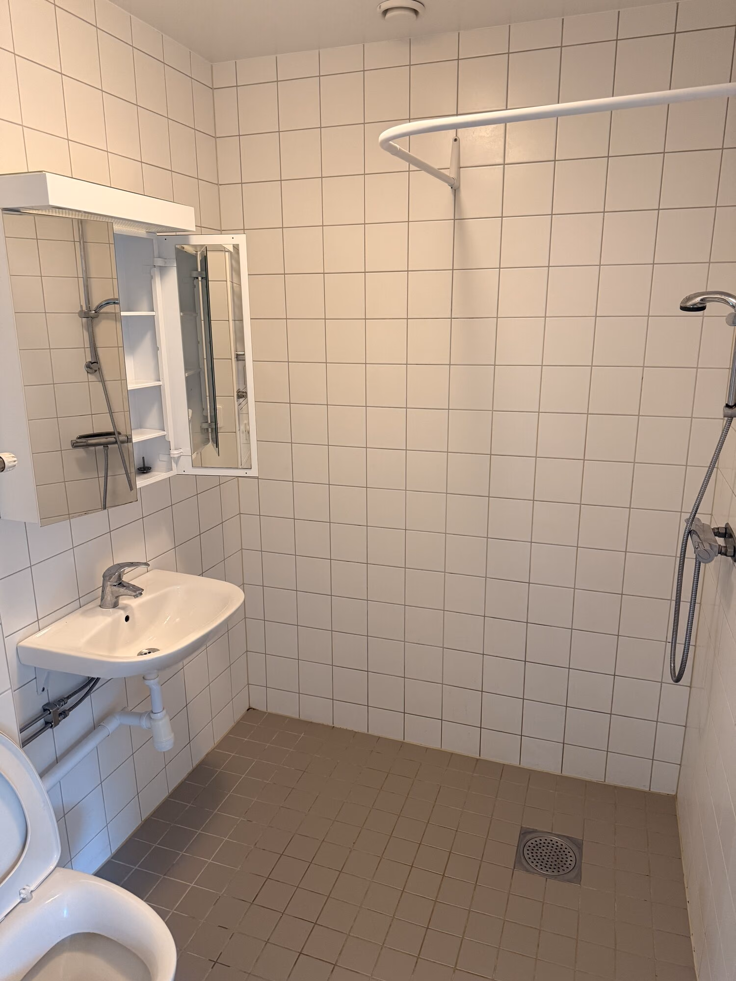 Nystädat tomt badrum med vitt kakel, handfat, spegelskåp och dusch