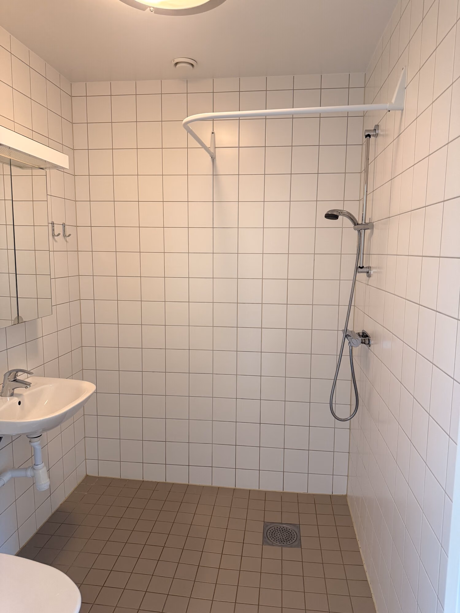 Rent tomt badrum med vitt kakel, brunt klinkergolv och duschblandare på väggen