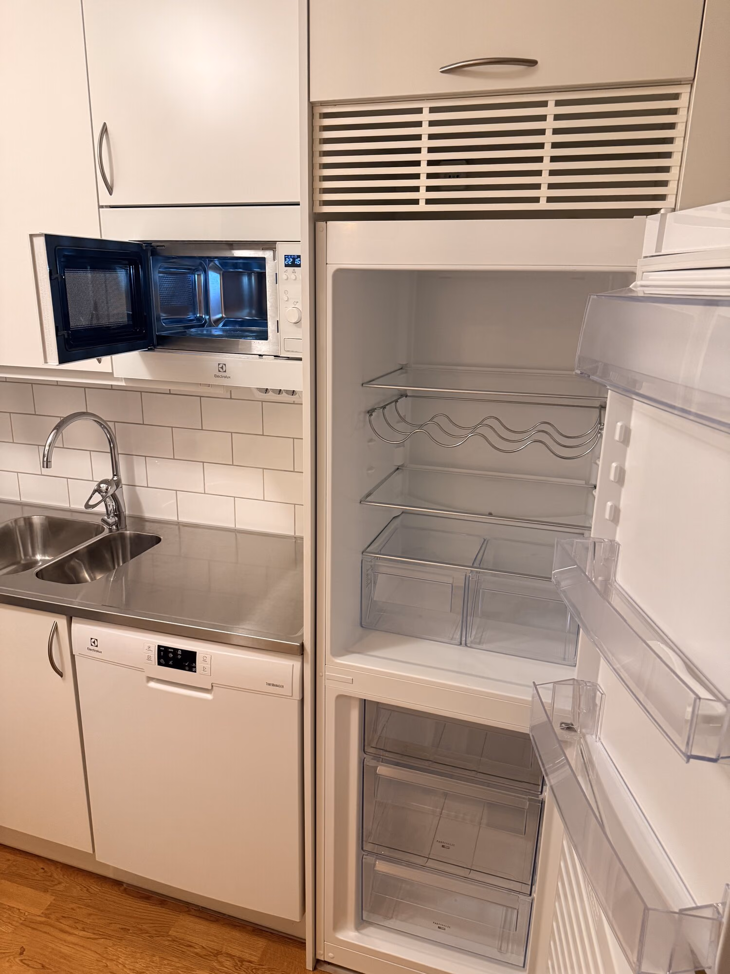 Öppet och urtorkat kylskåp och frys samt öppen mikrovågsugn i ett nystädat kök