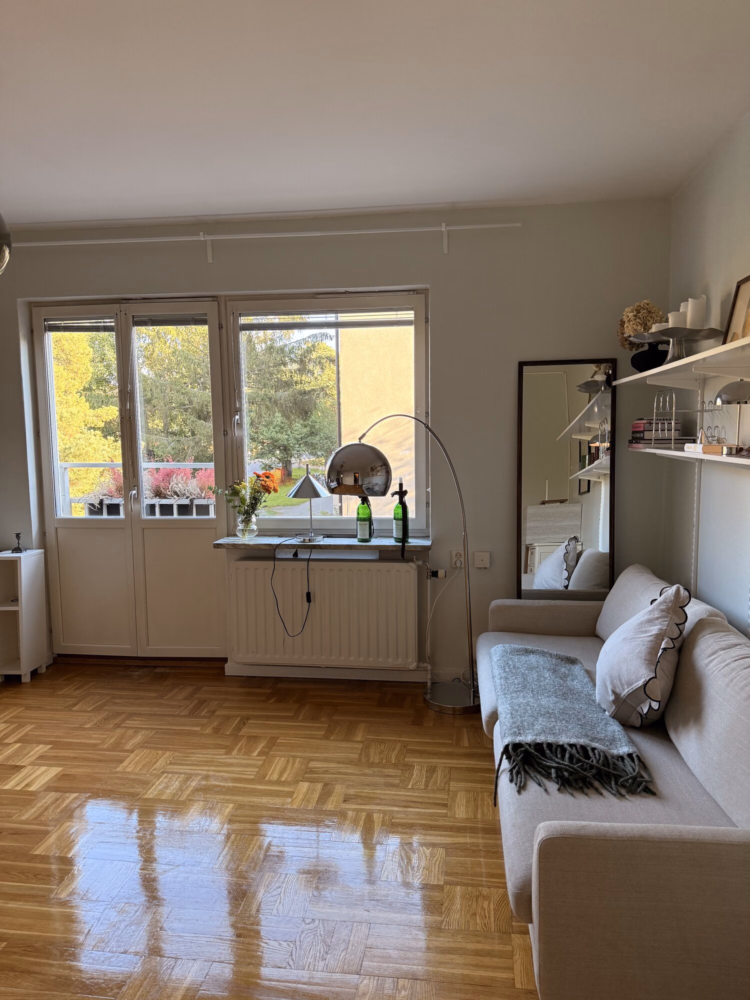 Vardagsrum med nyvårdat, blankt parkettgolv, beige soffa och balkongdörr med dagsljus